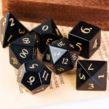 Black polyhedral dice set with gold numbers on a textured surface