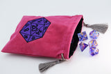A pink velvet D20 gaming bag with a purple embroidered D20 icon on the front, shown with several translucent purple polyhedral dice on a white background.