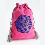 A pink velvet drawstring pouch with tassel ends, featuring a large embroidered purple 20-sided die on the front, set against a plain white background.