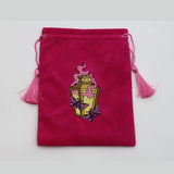 A small magenta velvet drawstring pouch with pink tassels and an embroidered yellow potion bottle design on the front, shown against a plain light gray background.