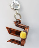Metallic charm shaped like a number '2' with a yellow bead on a white background