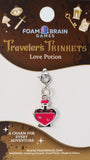 Charm for 'Traveler's Trinkets Love Potion' by Foam Brain Games on a brown card with decorative elements.