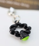 Black chain-like charm with a green accent on a white background