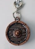 Bronze-colored circular pendant with intricate design on a gray background