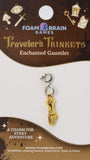 Gold charm on a 'Foam Brain Games' branded card with text about 'Traveler's Trinkets'.