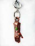 Copper hand charm with a green stone on a white background