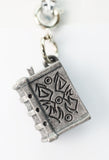 Silver book-shaped charm with decorative elements on a white background