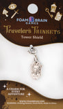 Silver charm on a Foam Brain Games card labeled 'Traveler's Trinkets Tower Shield'.
