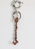 Copper charm shaped like a hook on a silver chain against a white background