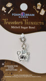 Silver charm for a traveler's trinkets set on Foam Brain Games packaging.