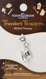 Silver teacup charm on a Foam Brain Games card with decorative elements.
