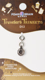 Traveler's Trinkets charm on a Foam Brain Games packaging with branding and product details.