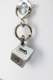 Silver charm shaped like a die with numbers on a white background