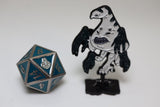 Metal polyhedral dice with blue and silver design next to a black and white figurine on a white background