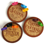 Three wooden coasters with engraved text and colorful clips on a white background