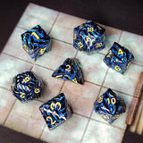 Set of metallic blue and black polyhedral dice with yellow numbers on a checkered surface.