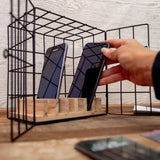 Person placing a smartphone into a black wire cage on a wooden surface.