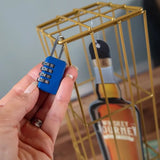 Hand holding a blue combination lock in front of a gold cage with a bottle of Journeyman Whiskey in the background.