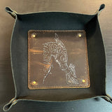 Black leather tray with a brown leather inset featuring an engraved design on a metallic surface.