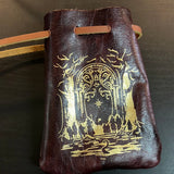 Brown leather pouch with gold embossed design on a dark background