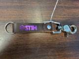 Keychain with 'STTH' logo on a wooden surface