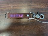 Brown leather keychain with 'THIS IS THE WAY' text on a wooden surface