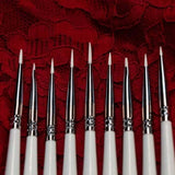 Set of white nail art brushes with silver ferrules on a red lace background