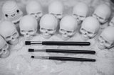 Makeup brushes on a textured surface with small skull-like figures in the background