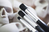 Makeup brushes with a skull-shaped object in the background