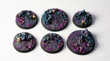 Six round miniature bases with colorful terrain and skull designs on a white background