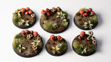 Six round miniature bases with terrain and plant decorations on a white background