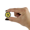 A hand with dark nail polish holds a Beyblade toy against a plain white background. The Beyblade features a bright yellow center with a black star emblem, surrounded by a silver and black outer ring.