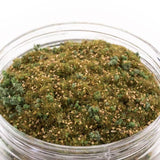 Glass jar filled with a mix of green and brown moss-like material on a white background