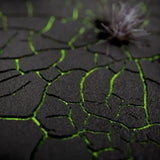 Close-up of a textured black surface with green lines and a small plant in the corner.