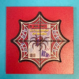 Decorative patch with spider design and 'Little Shop of Magic' text on a red background