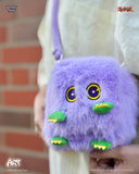 Purple fluffy bag with cartoonish face held by a person against a brick wall.