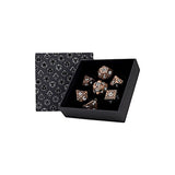 Set of rose gold dice with black pips in a black box with geometric patterned lid on a white background