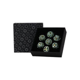 Set of six green dice with metallic sheen in a black box with geometric pattern