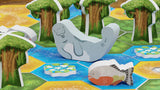 Board game piece of a whale on a colorful game board with trees and water.