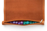 Brown zipper pouch with colorful polyhedral dice inside on a white background