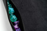 Close-up of a black zipper pouch with green and purple polyhedral dice inside.