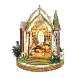 A miniature gothic-style decorative building kit with a lit interior, arched windows, floral details, small figurines, and a brick base, shown on a plain white background.