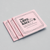 Three copies of the board game 'The Love Ballon' are arranged in a fan-like stack on a light gray textured background. The game box features a light pink cover with black text and geometric line art.