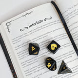 Black and gold dice set on an open book with 'interlude' text