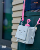 Gray plush bag with pink handle, resembling a cube worn by a person.