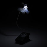 A gothic-themed desk lamp shaped like a floating white ghost with a black eye, mounted on a flexible gooseneck stand. The stand is a black book-shaped base featuring the title 'The Nightmare Before Christmas' in white gothic lettering.