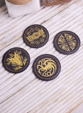 Four round black coasters with gold-colored fire element symbols, arranged on a light-colored wooden surface.