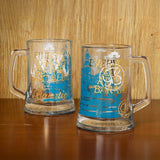 Two glass mugs with blue and gold designs on a wooden surface.