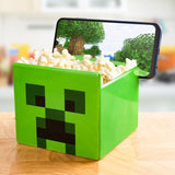 Green popcorn container with a face design on a wooden surface, filled with popcorn.