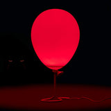 A red balloon-shaped table lamp glowing in the dark, with a thin stem and cord on a black background.